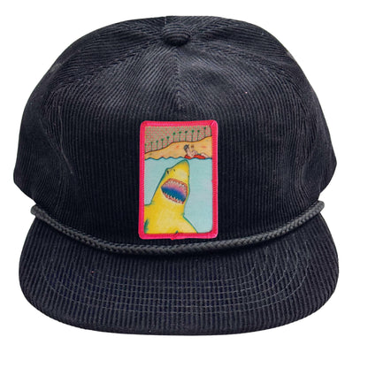 Black corduroy cap with a colorful patch featuring a shark and a person on a surfboard.